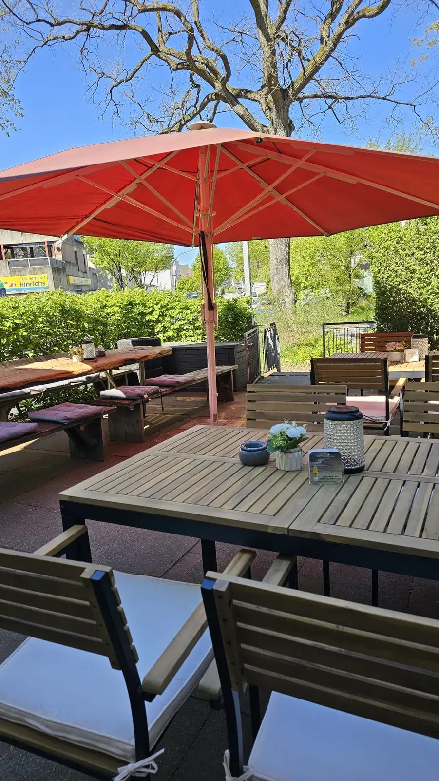 Die Terrasse mit Holztischen und roten Sonnenschirmen